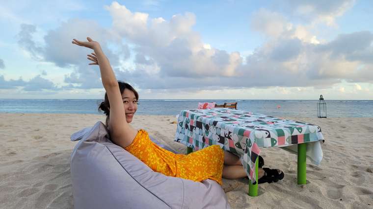 Ixchel on a beach in Bali in 2022, smiling with one arm raised — one of her own trips.